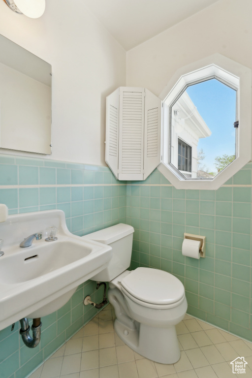 Bathroom featuring tile walls, toilet, tile patterned floors, a sink, and wainscoting