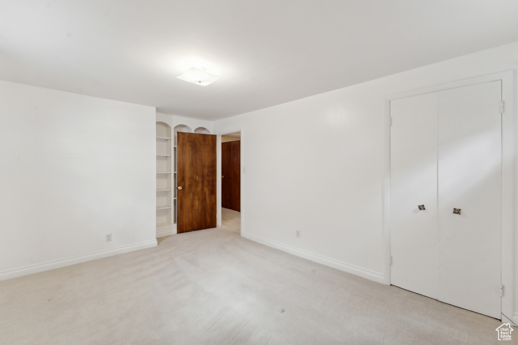 Unfurnished bedroom featuring a closet, light colored carpet, and baseboards