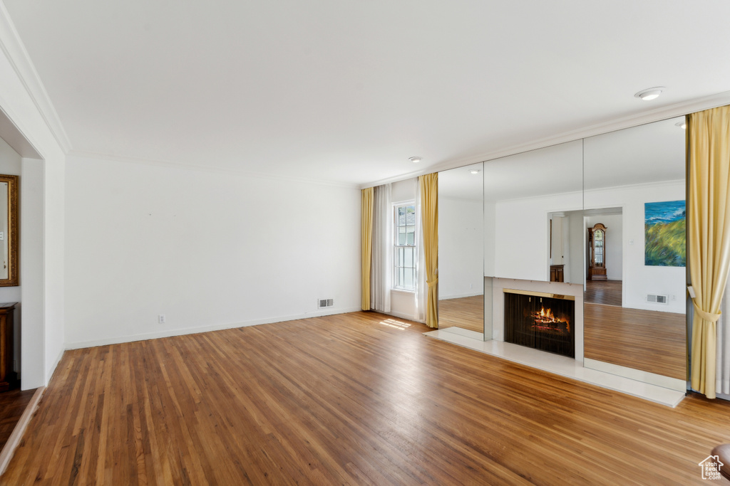 Unfurnished living room with wood finished floors, crown molding, a warm lit fireplace, and baseboards