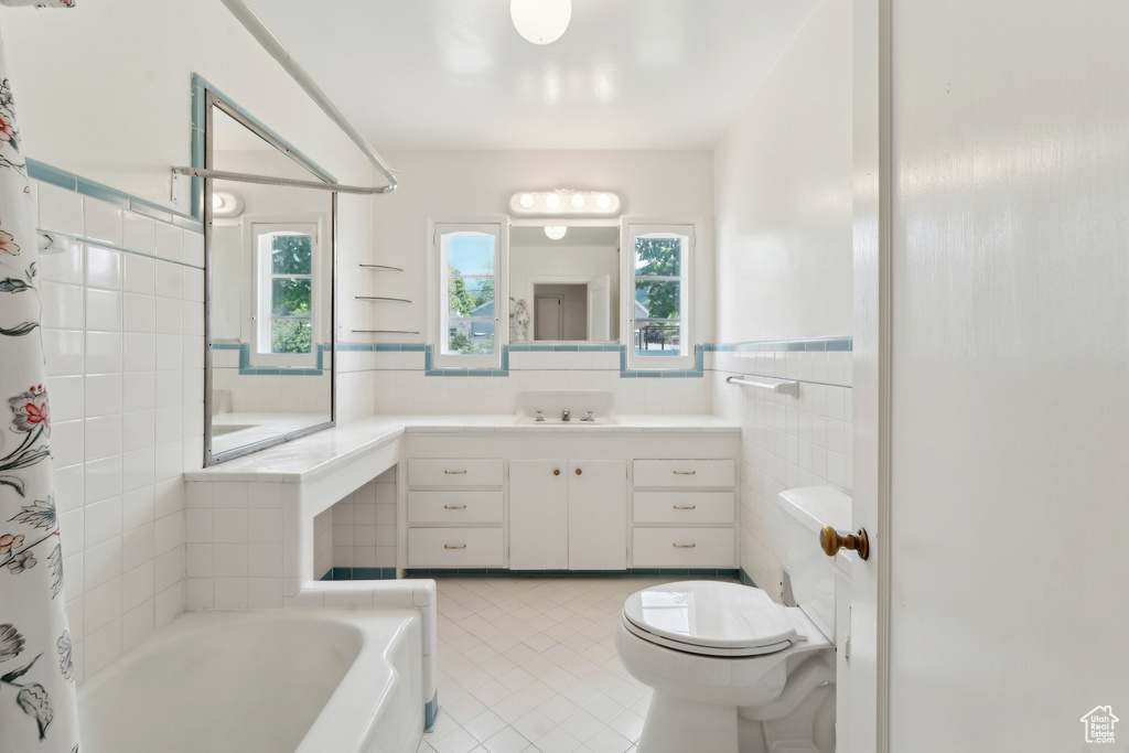 Bathroom featuring tile patterned flooring, a tub, toilet, plenty of natural light, and tile walls