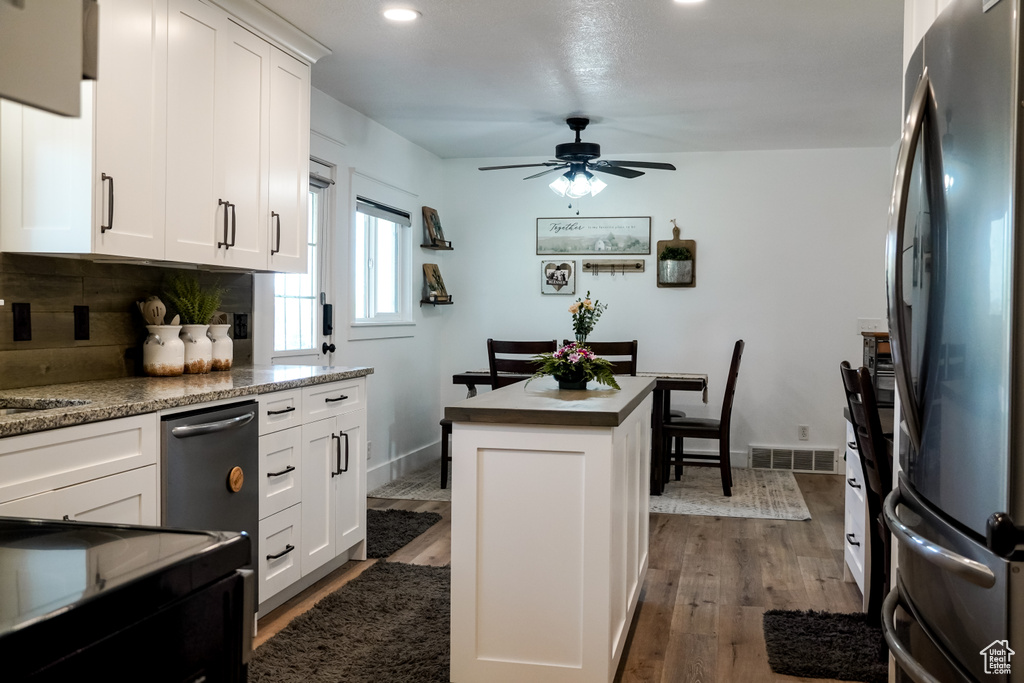 Kitchen featuring freestanding refrigerator, a center island, decorative backsplash, a ceiling fan, and dark wood-type flooring