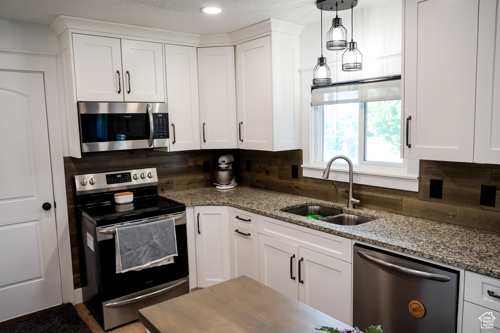 Kitchen with appliances with stainless steel finishes, a sink, tasteful backsplash, white cabinetry, and light stone countertops