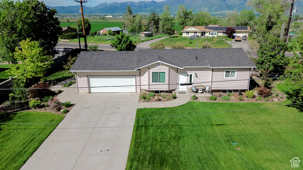 Ranch-style home featuring concrete driveway, a mountain view, a front yard, and an attached garage