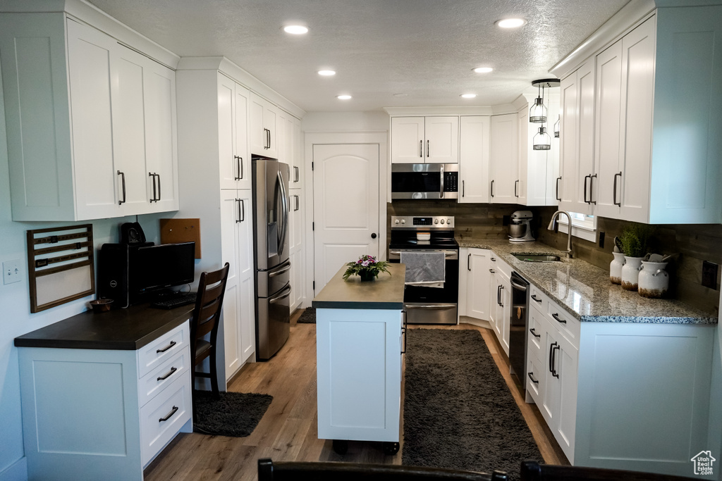 Kitchen with appliances with stainless steel finishes, a sink, white cabinets, a center island, and recessed lighting