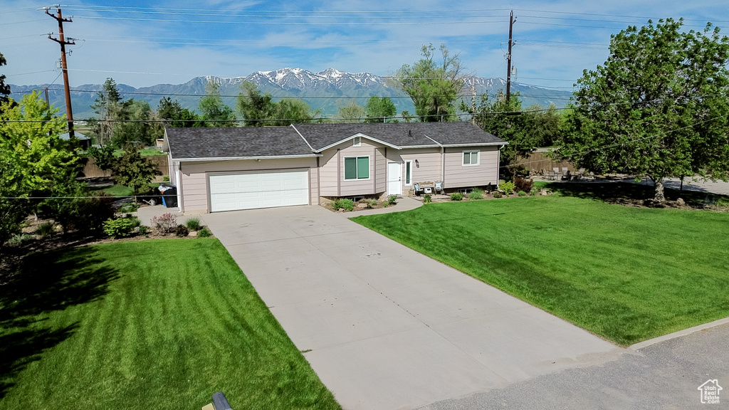 Single story home with a front lawn, concrete driveway, a mountain view, and a garage