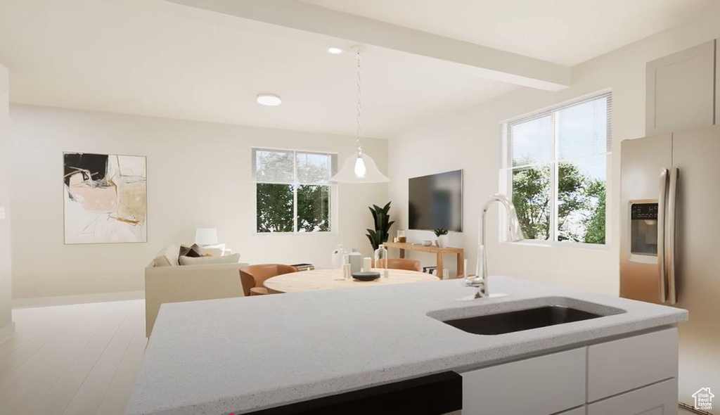 Kitchen featuring stainless steel refrigerator with ice dispenser, a sink, hanging light fixtures, open floor plan, and light stone countertops