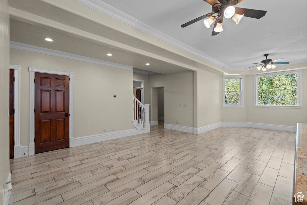 Spare room featuring a ceiling fan, stairway, light wood-type flooring, crown molding, and baseboards