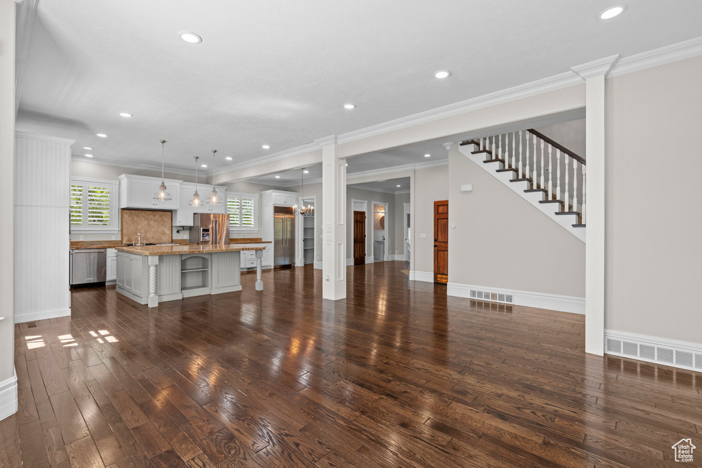 Unfurnished living room featuring dark wood-type flooring, recessed lighting, a sink, crown molding, and baseboards
