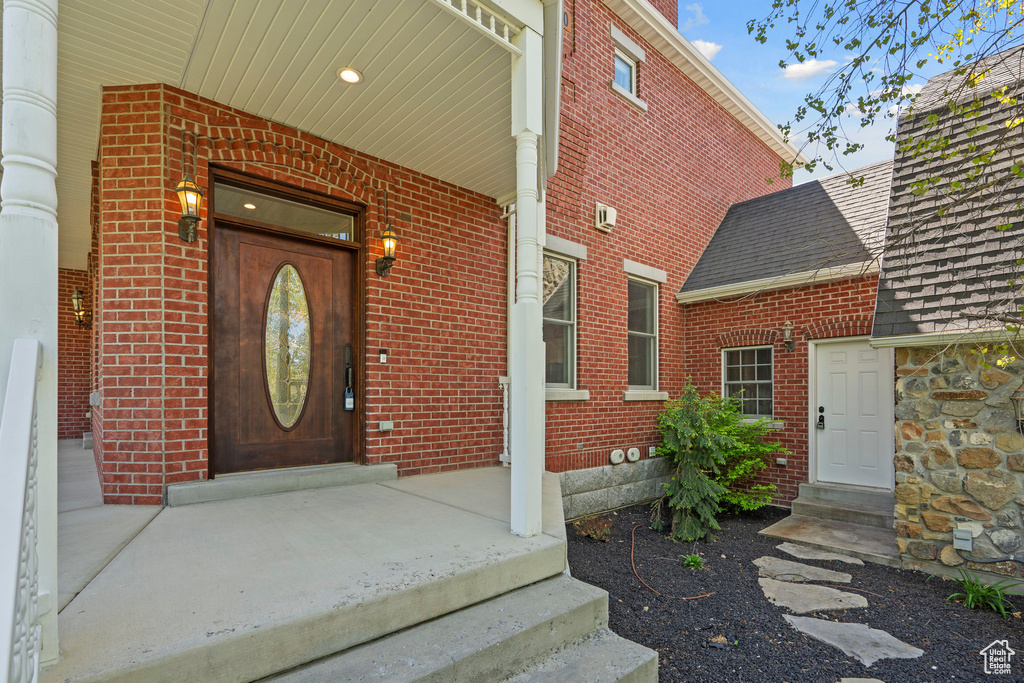 Property entrance featuring brick siding, a shingled roof, and a porch