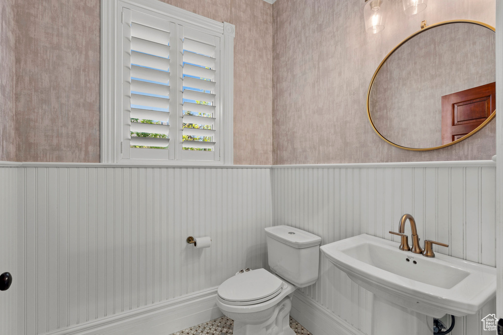 Half bathroom with wainscoting, toilet, a sink, and wallpapered walls