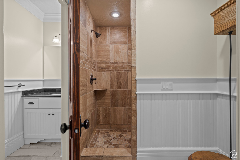 Full bathroom featuring a tile shower, ornamental molding, vanity, and marble look tile flooring