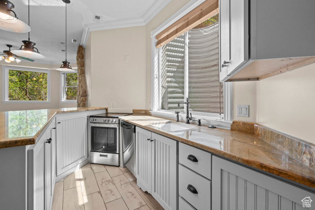 Kitchen with a sink, appliances with stainless steel finishes, ornamental molding, ceiling fan, and light stone countertops