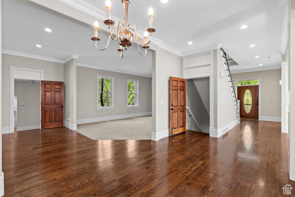 Unfurnished living room featuring wood-type flooring, recessed lighting, baseboards, a chandelier, and ornamental molding
