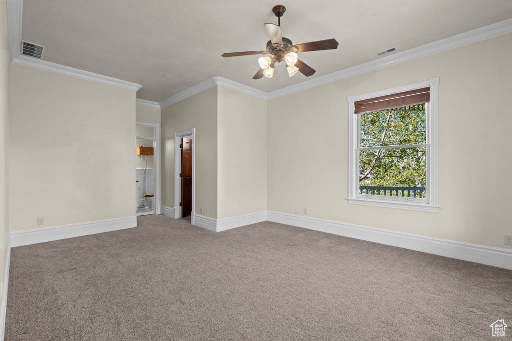 Carpeted spare room featuring a ceiling fan, crown molding, and baseboards