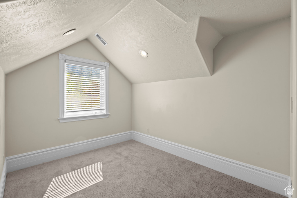 Bonus room featuring a textured ceiling, carpet, lofted ceiling, and baseboards