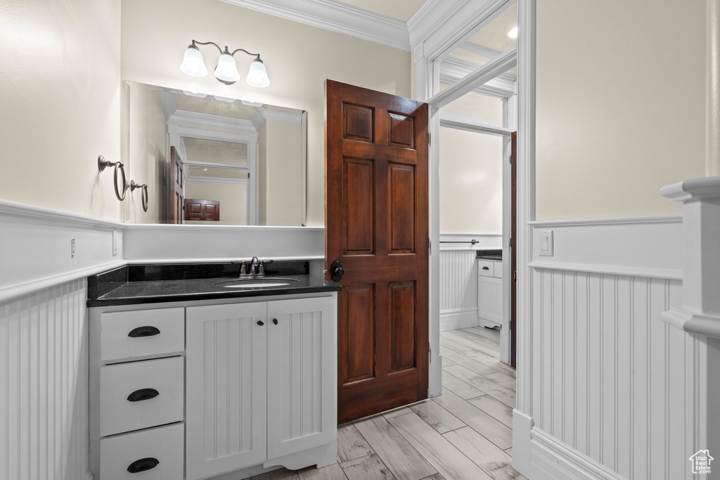 Bathroom featuring crown molding, a wainscoted wall, vanity, and a decorative wall
