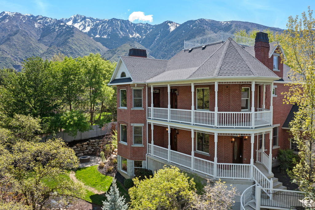 View of front of property with a chimney, a balcony, brick siding, a mountain view, and a porch