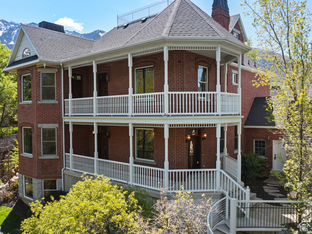 View of front facade featuring a balcony, brick siding, a shingled roof, and a porch