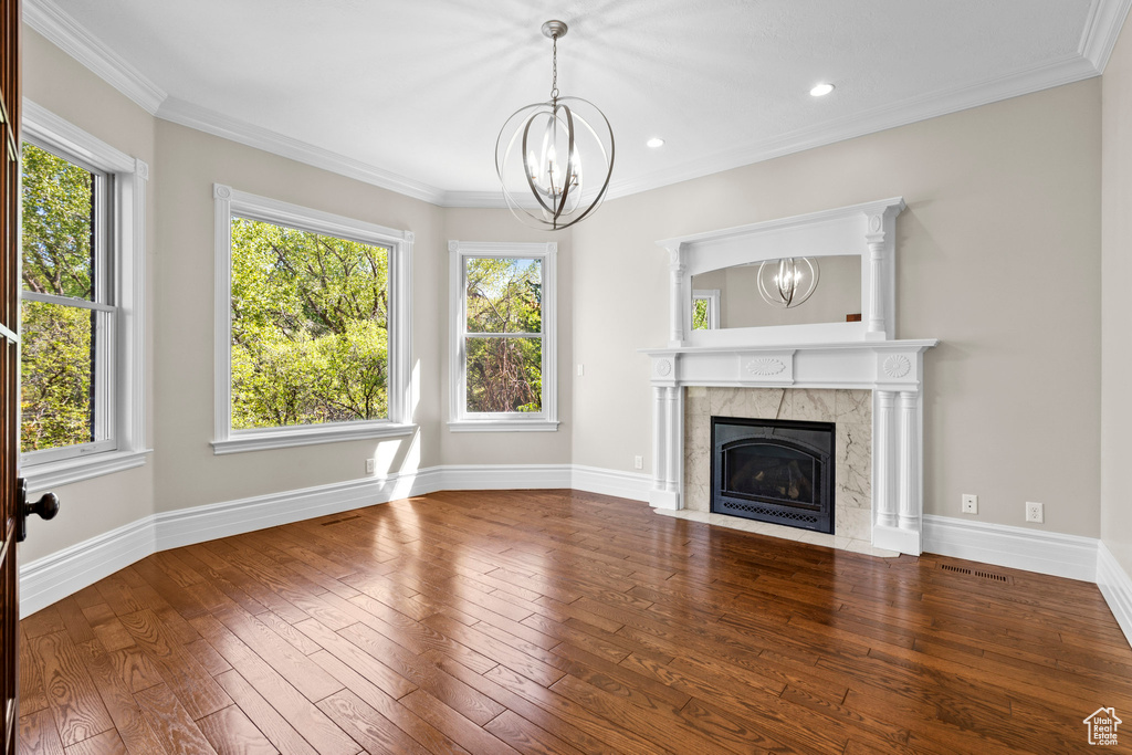 Unfurnished living room featuring a chandelier, wood-type flooring, plenty of natural light, crown molding, and baseboards