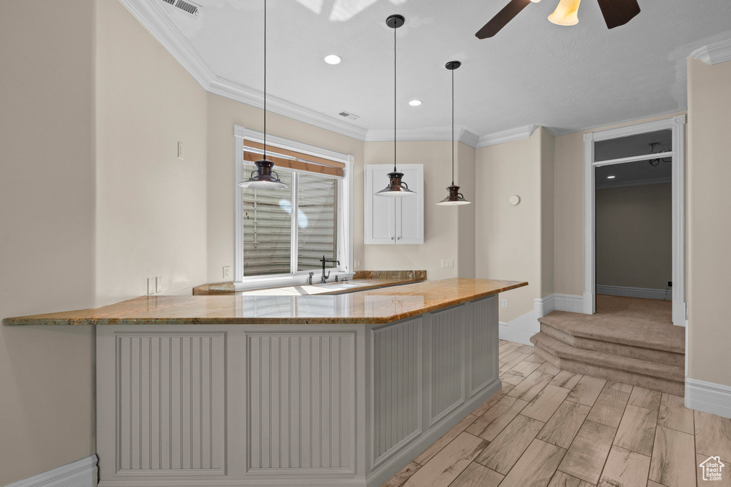 Kitchen with crown molding, baseboards, a sink, light stone counters, and a ceiling fan