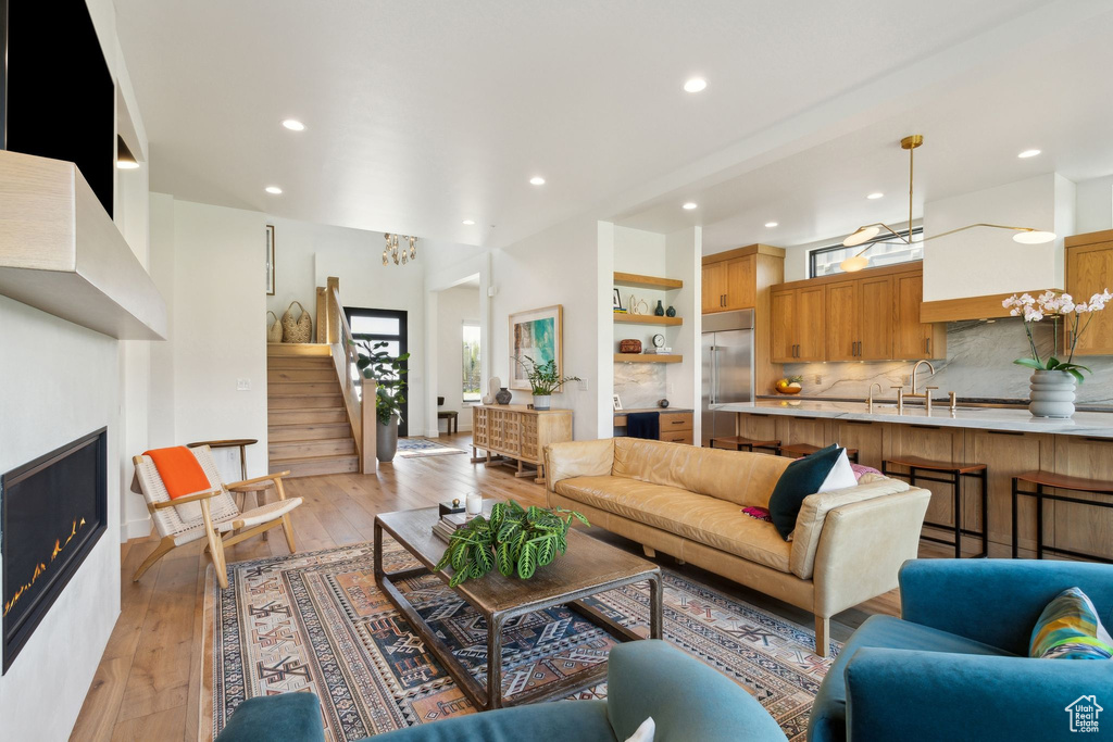 Living area featuring recessed lighting, stairway, a warm lit fireplace, and light wood-style floors