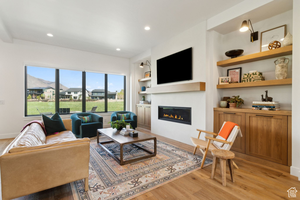 Living room featuring a glass covered fireplace, light wood-style floors, recessed lighting, and built in features