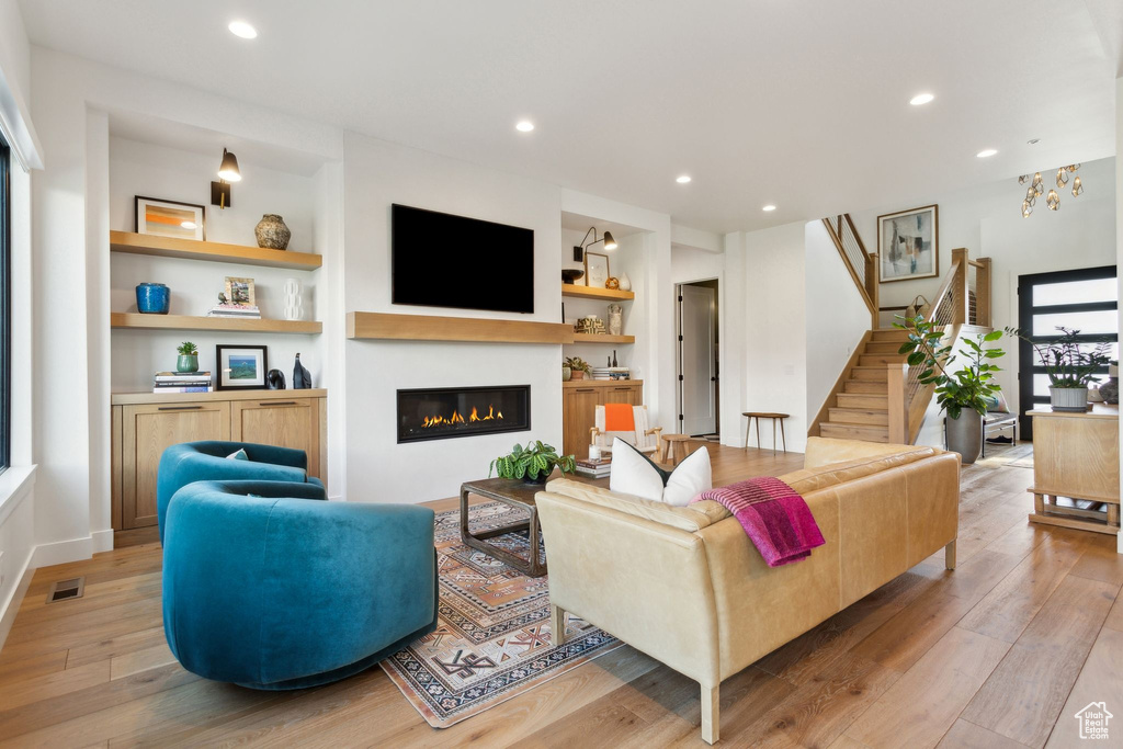 Living area featuring light wood-style flooring, stairs, a glass covered fireplace, recessed lighting, and built in features