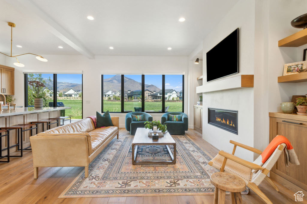 Living room with a glass covered fireplace, light wood finished floors, recessed lighting, and beamed ceiling