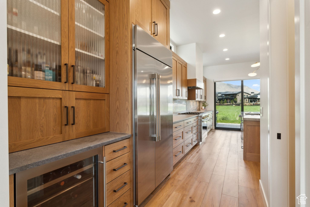Kitchen with high end appliances, beverage cooler, light wood-type flooring, glass insert cabinets, and recessed lighting