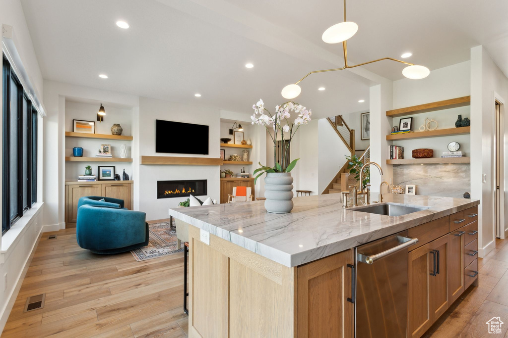 Kitchen with a sink, a glass covered fireplace, open shelves, light stone counters, and light wood finished floors