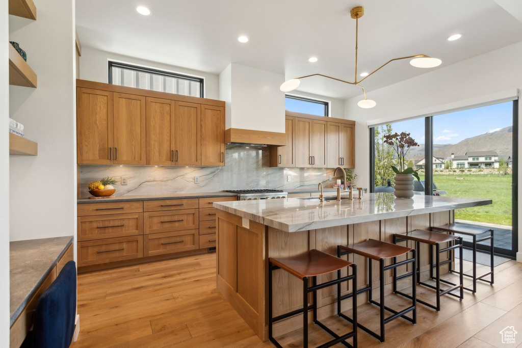 Kitchen with decorative backsplash, a sink, a kitchen island with sink, a breakfast bar area, and light stone countertops