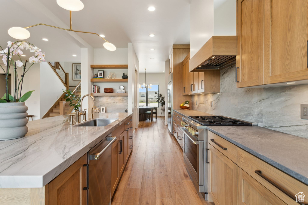 Kitchen with high quality appliances, a sink, wall chimney range hood, open shelves, and light stone counters