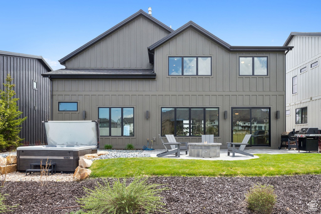 Back of property featuring a fire pit, a patio area, board and batten siding, and a hot tub