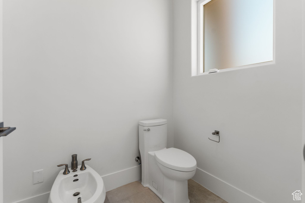 Bathroom with toilet, baseboards, tile patterned flooring, and a bidet