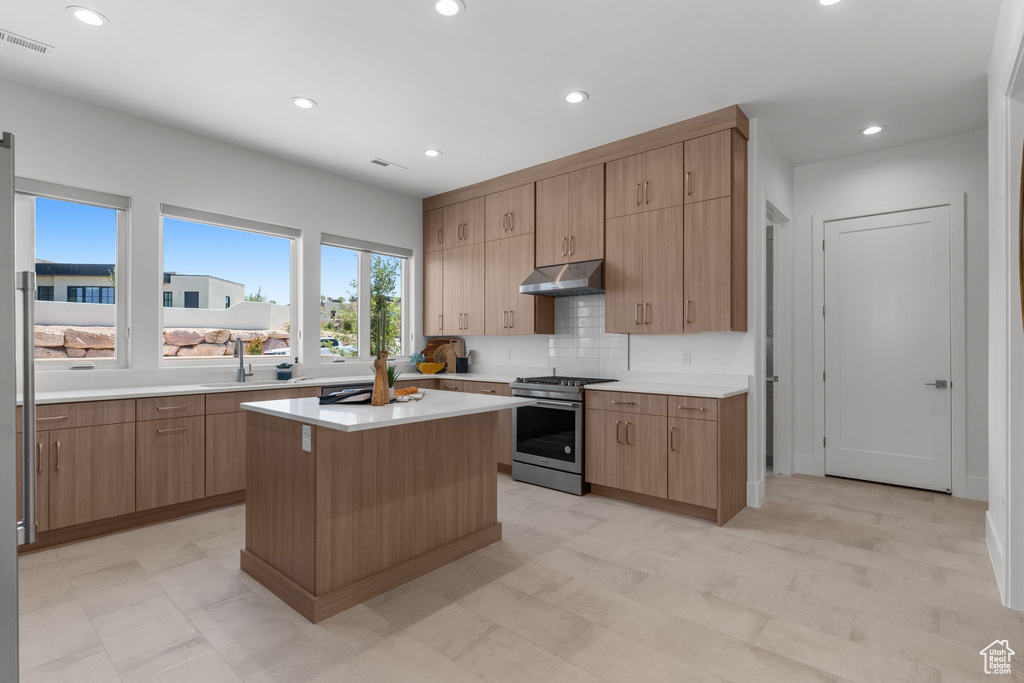 Kitchen featuring gas stove, under cabinet range hood, light countertops, a sink, and a kitchen island