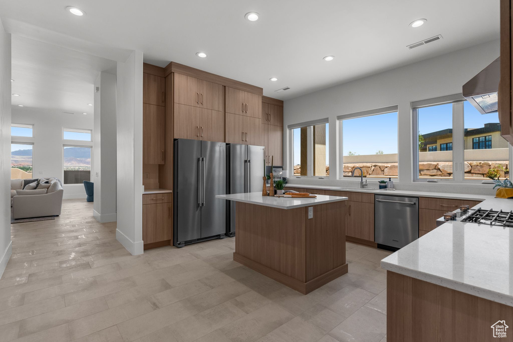 Kitchen featuring stainless steel appliances, modern cabinets, a sink, wall chimney exhaust hood, and light stone countertops