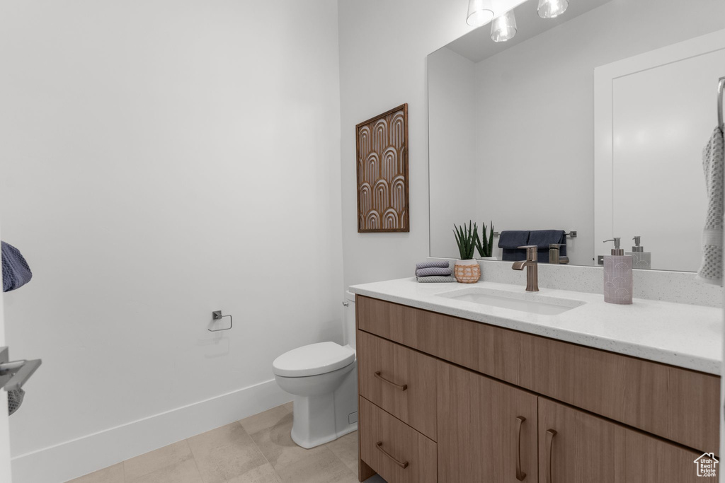 Half bathroom with vanity, toilet, baseboards, and tile patterned floors