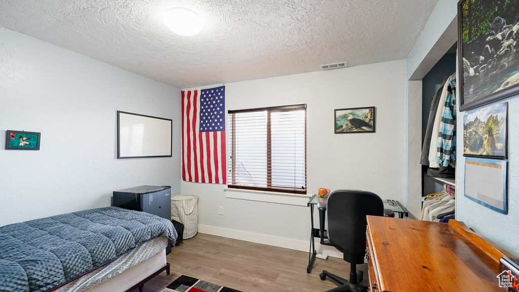 Bedroom featuring a textured ceiling, wood finished floors, a desk, and baseboards