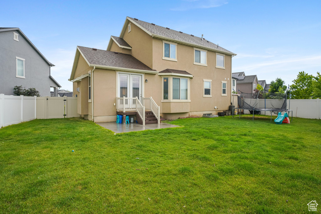 Rear view of house featuring a trampoline, stucco siding, a patio area, and a shingled roof