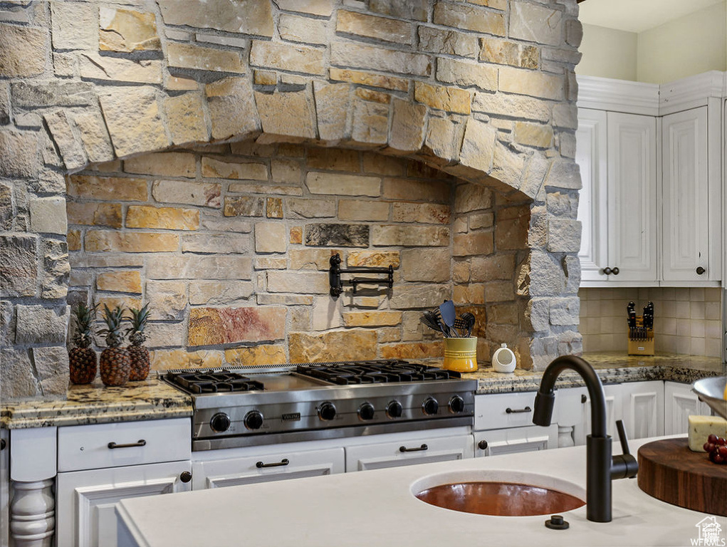 Kitchen featuring a sink, light stone countertops, stainless steel gas stovetop, white cabinets, and decorative backsplash