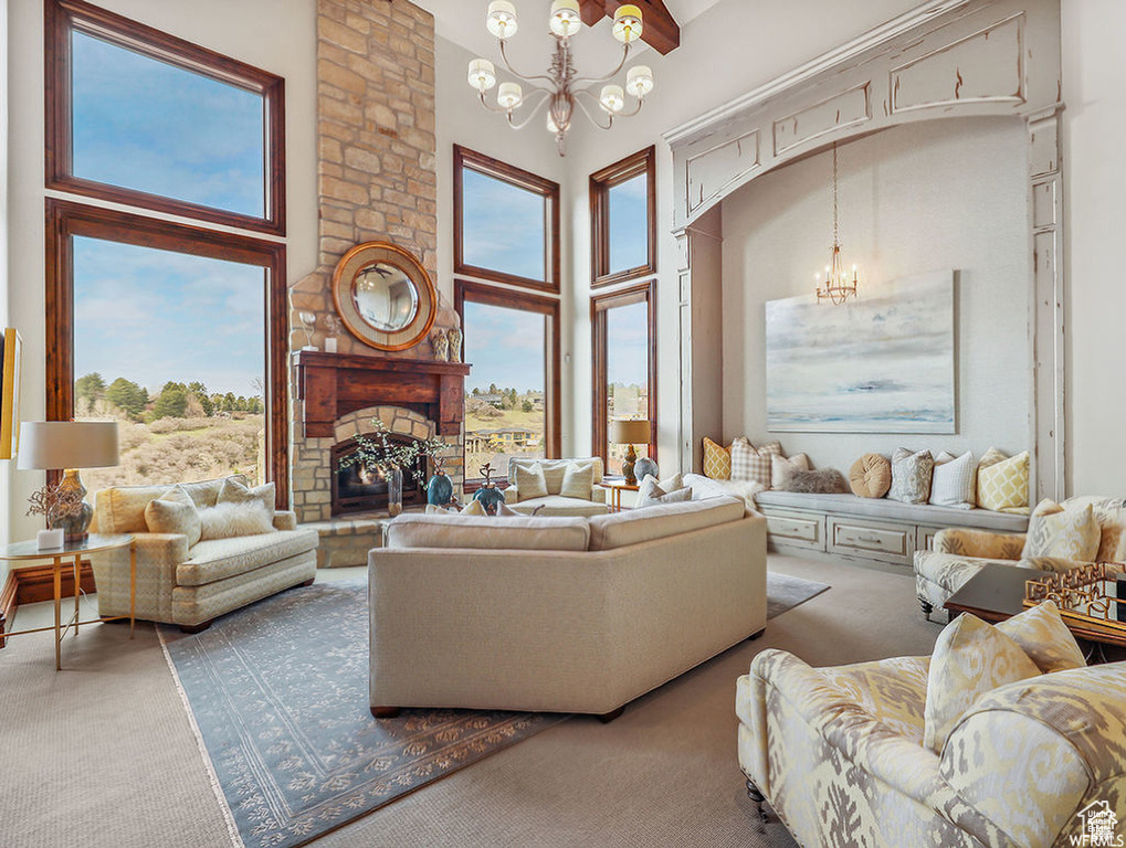 Carpeted living area with a stone fireplace, a towering ceiling, and a chandelier