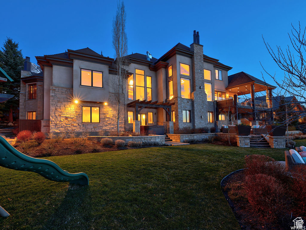 Rear view of house featuring stone siding, a chimney, stucco siding, a yard, and a playground