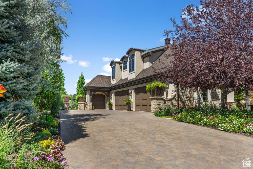 View of side of property with stone siding, stucco siding, decorative driveway, and a garage