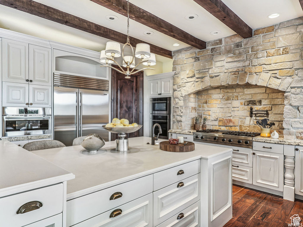 Kitchen with white cabinetry, hanging light fixtures, a kitchen island with sink, and appliances with stainless steel finishes