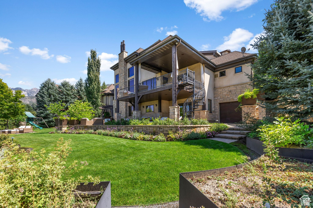 Back of house with stucco siding, an attached garage, stone siding, a playground, and a yard