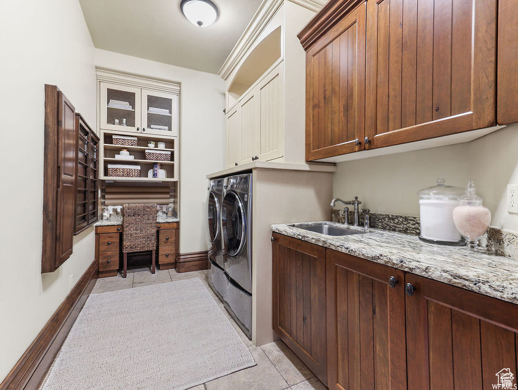 Laundry room featuring light tile patterned flooring, washing machine and dryer, a sink, baseboards, and cabinet space