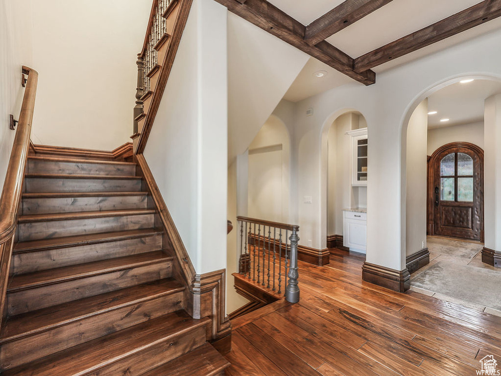 Stairway featuring arched walkways, beam ceiling, recessed lighting, and wood-type flooring