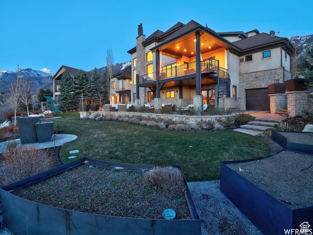 Back of property featuring stone siding, a garage, stucco siding, a mountain view, and a yard