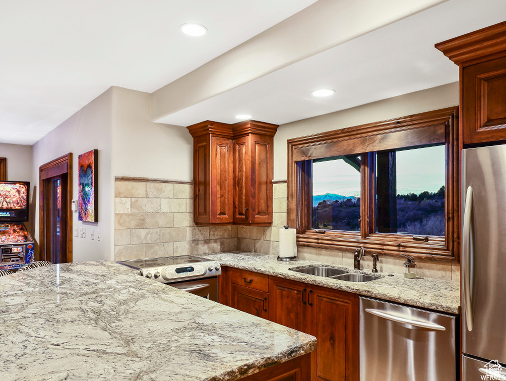 Kitchen with a sink, backsplash, appliances with stainless steel finishes, and light stone counters
