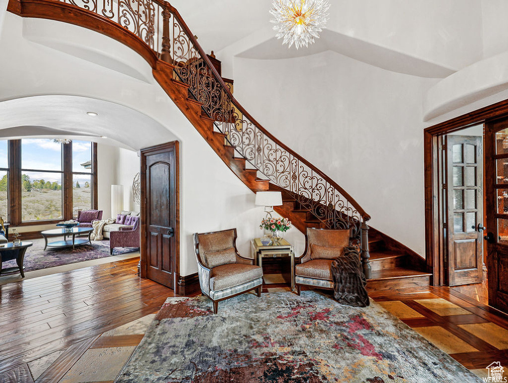 Living room with stairs, wood-type flooring, an inviting chandelier, a high ceiling, and arched walkways